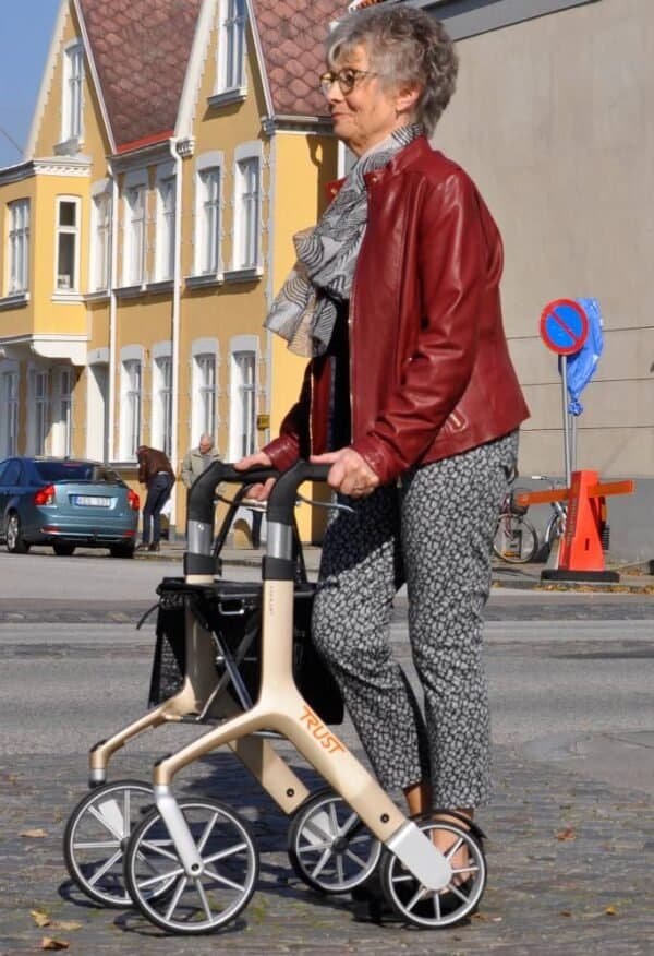 Äldre kvinna promenerar med modern rollator från Trust på stadsgata en solig dag – inspiration för dig som ska köpa rollator.