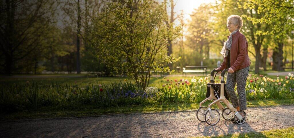 Senior som promenerar med rollator i park – hjälpmedel från Assistansbutiken